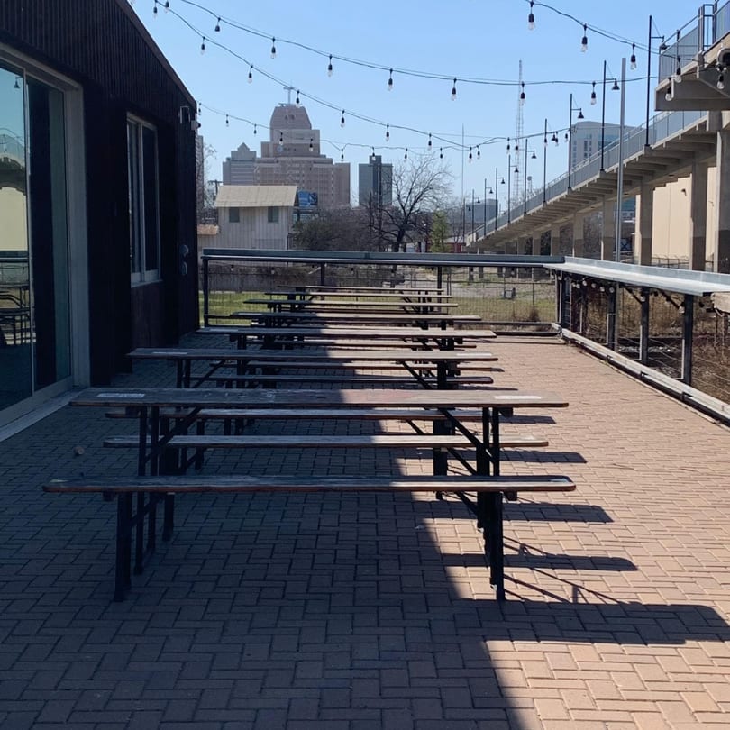 Outdoor patio with rows of picnic tables, string lights, and a city skyline in the background.