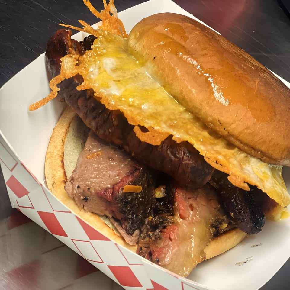 A Street Food Kings Mexican hot dog with brisket, sausage, and melted cheese in a paper tray.