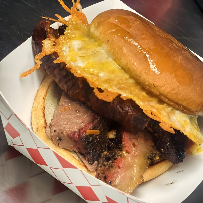 A Street Food Kings Mexican hot dog with brisket, sausage, and melted cheese in a paper tray.