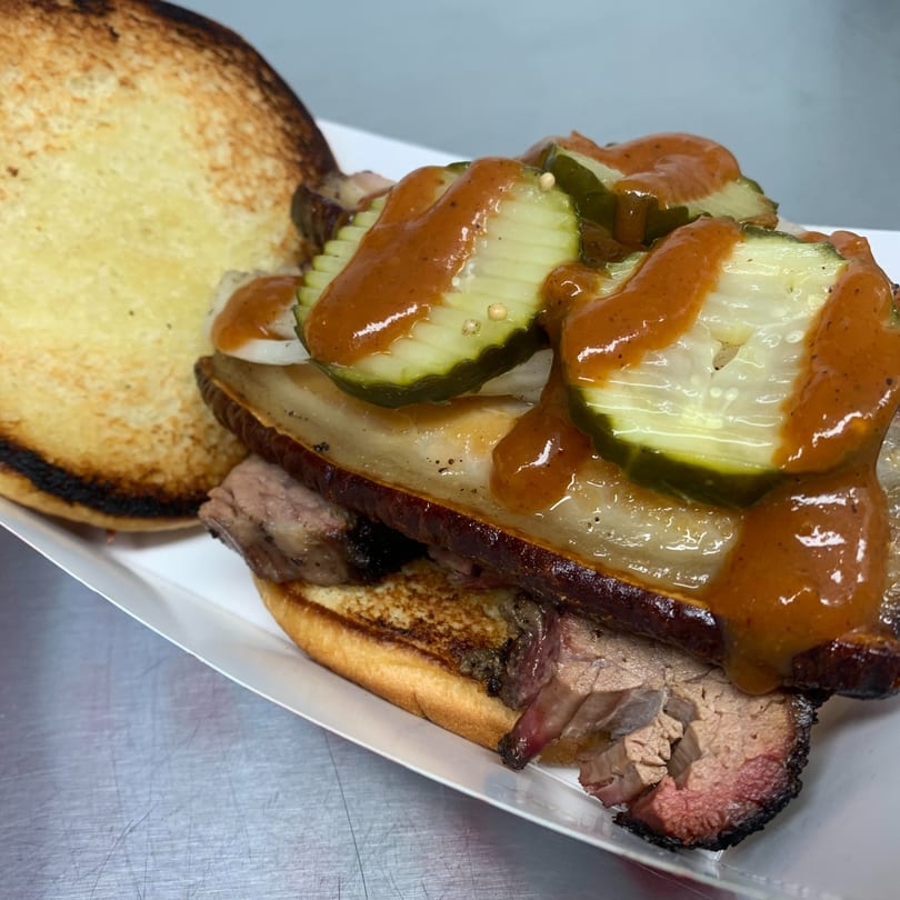 A Street Food Kings Mexican sandwich with brisket, pickles, and sauce on a toasted bun.
